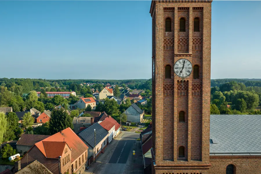 Ceglana wieża kościoła z zegarem nad zabudową wsi, widok z lotu ptaka
