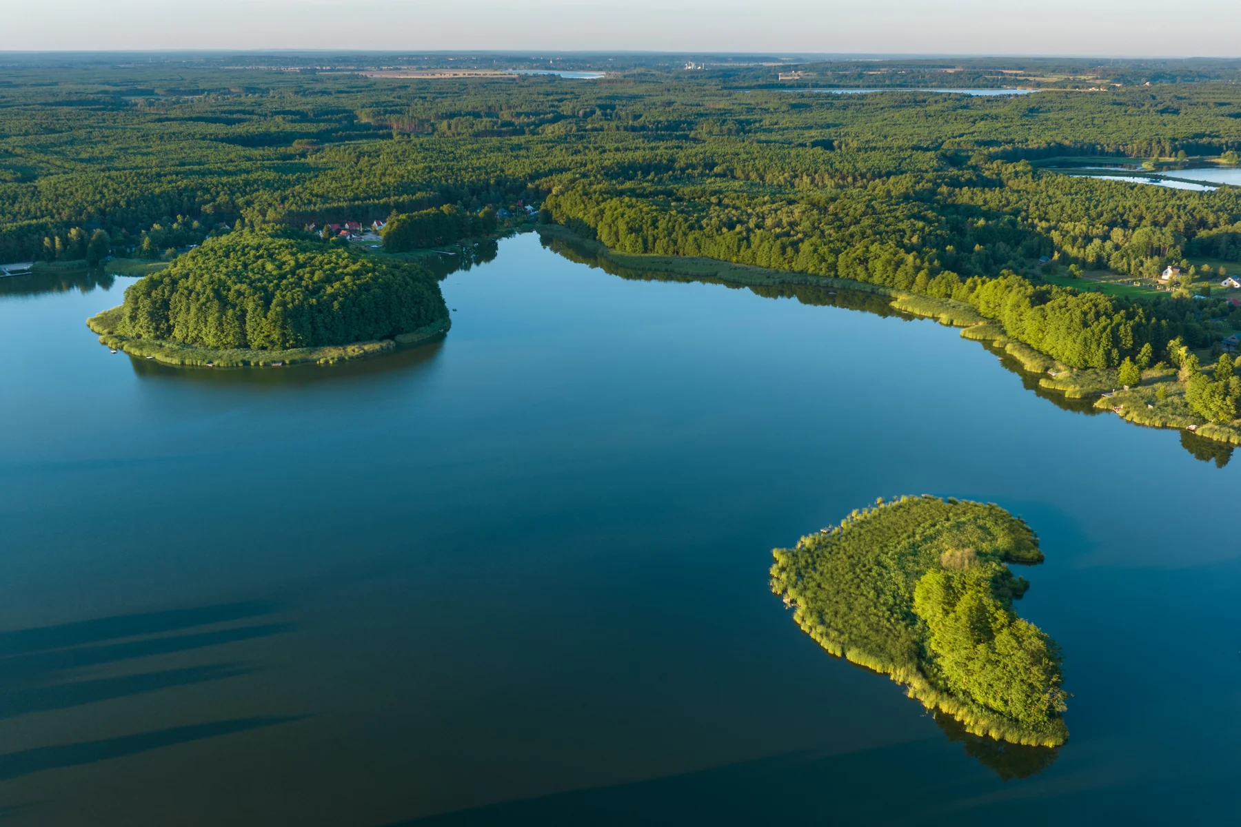 Jezioro o ciemnobłękitnej tafli z zalesioną wyspą i cyplem, lasy wokół brzegów, drugi akwen w oddali